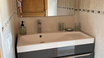 Une salle de bain avec une porte en bois, un lavabo blanc avec un robinet noir et un miroir au-dessus.