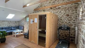 Una habitación con pared de piedra, vigas de madera, una cinta de correr, un armario de madera, un sofá y una pequeña mesa.