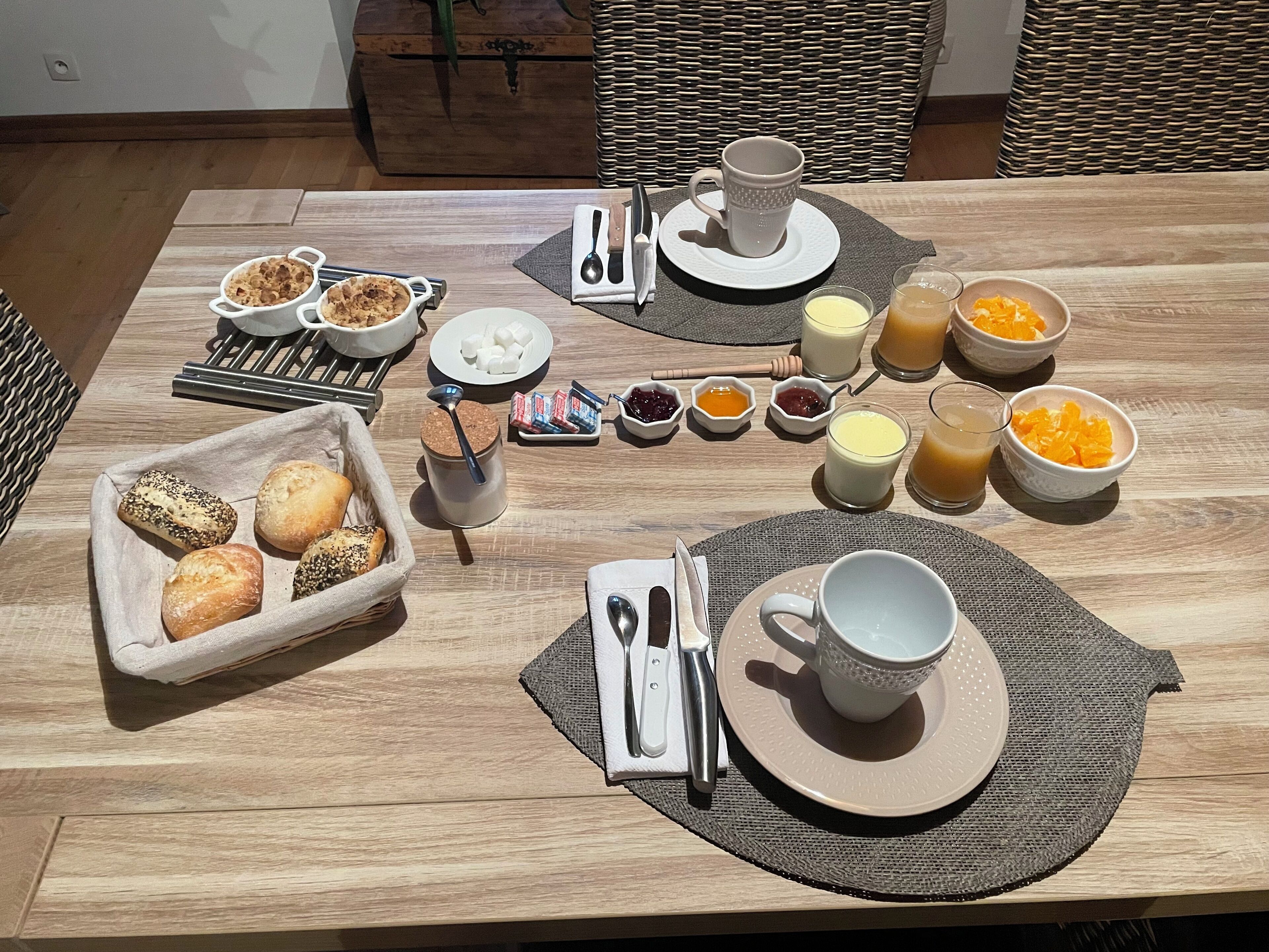 Una mesa de desayuno con pan, bollería, mermelada, miel y zumo de naranja.