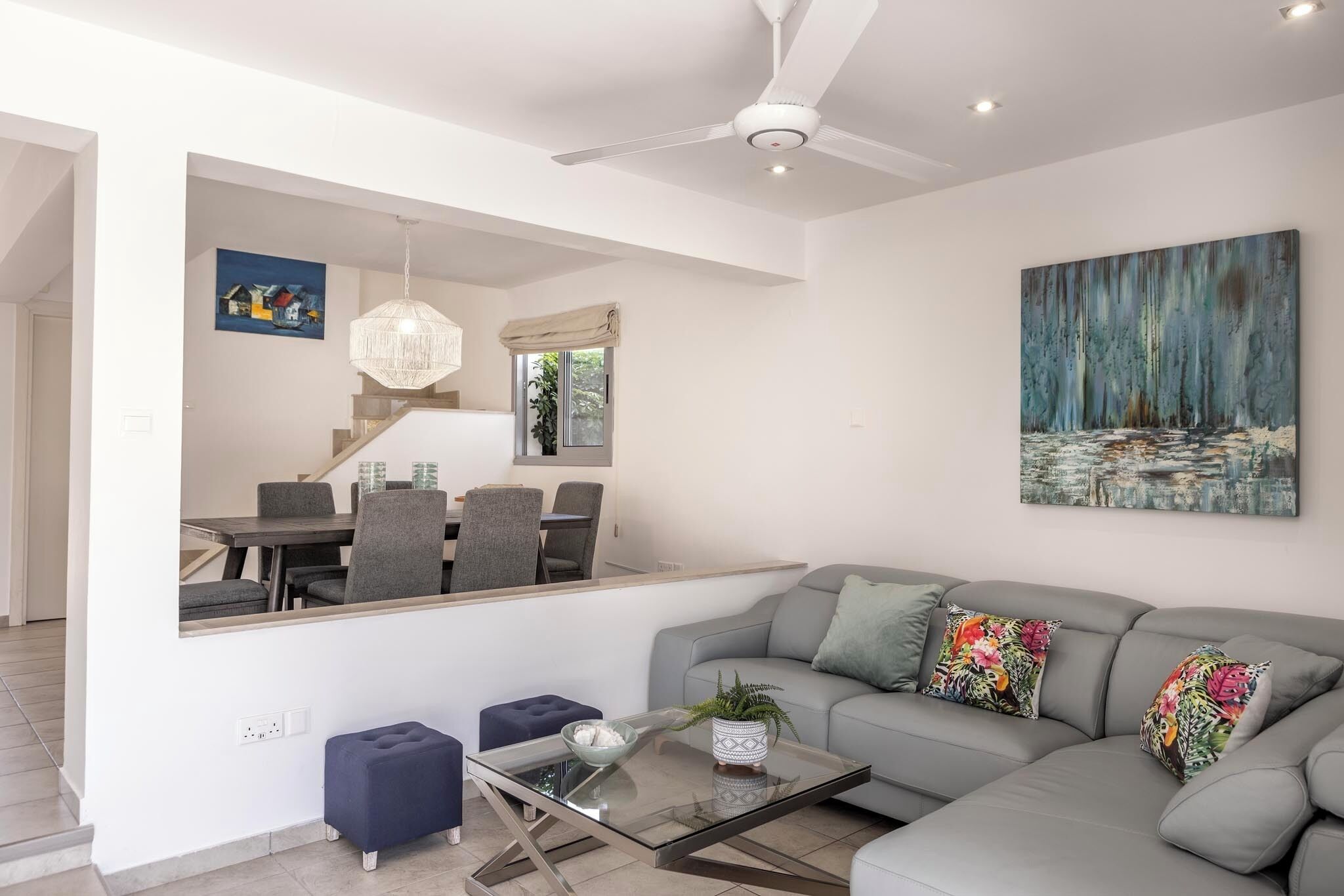 A modern living room with a gray sofa, a glass coffee table, and a large mirror reflecting the dining area.