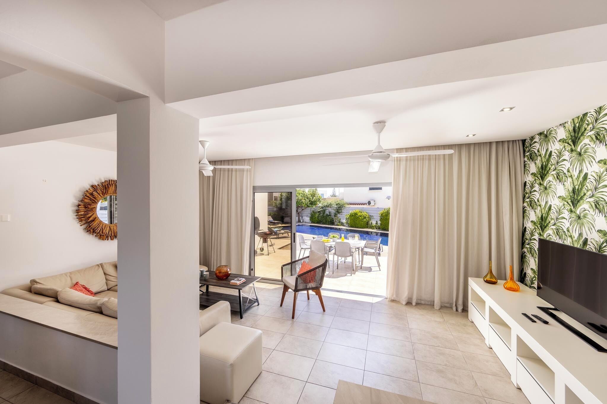 Ein modernes Wohnzimmer mit Sofa, Couchtisch und TV-Schrank. Ein Schiebetürfenster führt zu einer Außenpatio mit Pool.