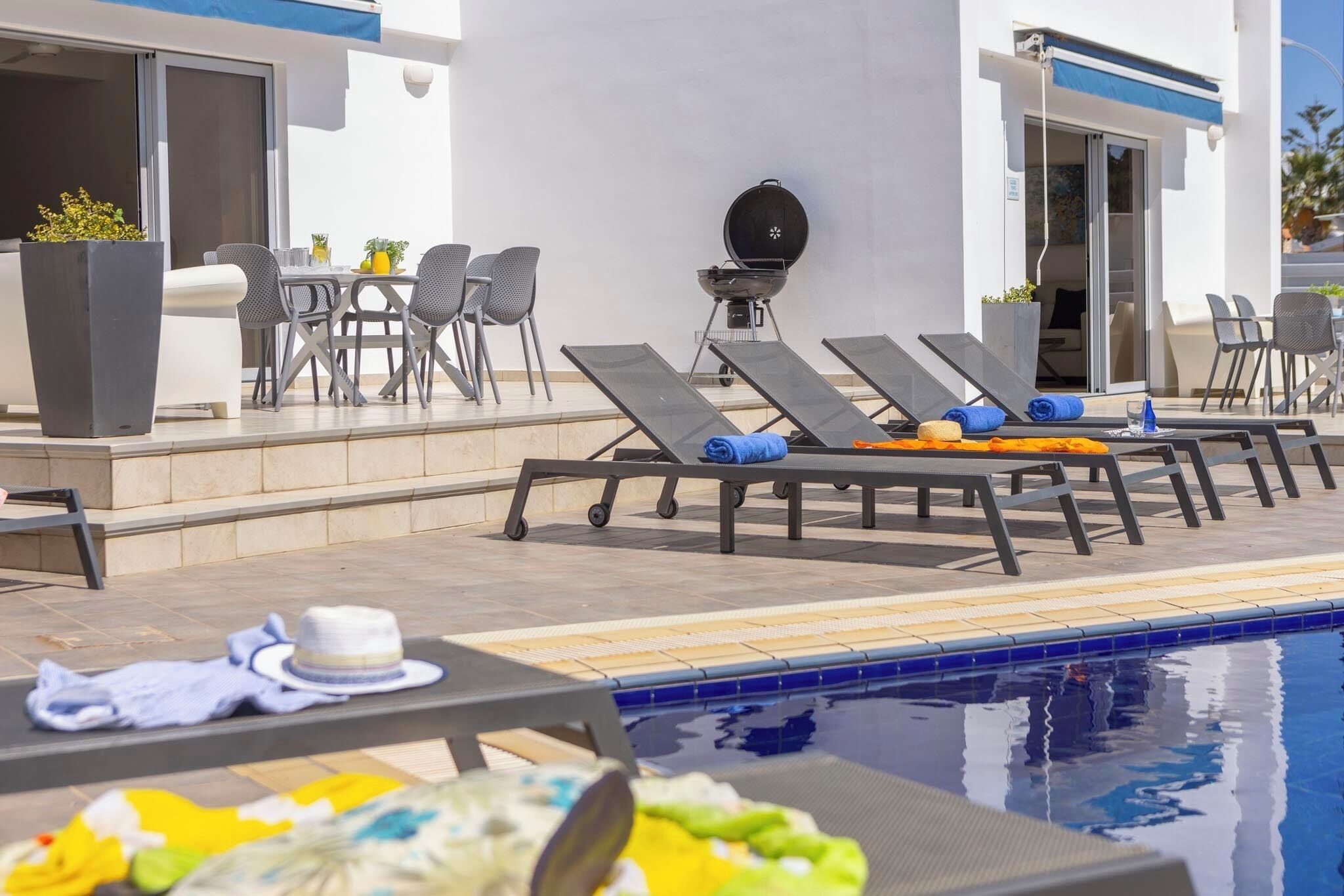 A poolside area with lounge chairs, a barbecue grill, and a dining setup.