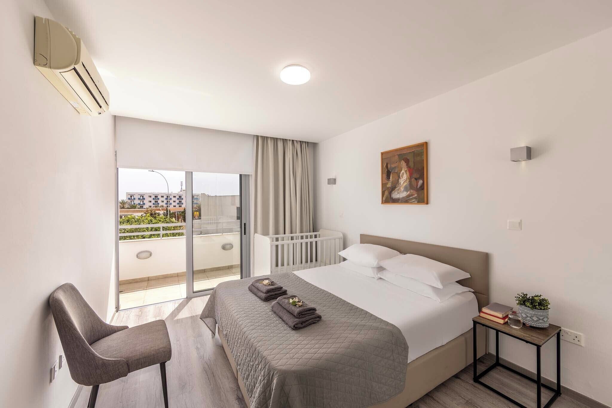 Habitación de hotel con cama, una silla, mesita de noche, un cuadro y vistas al exterior.