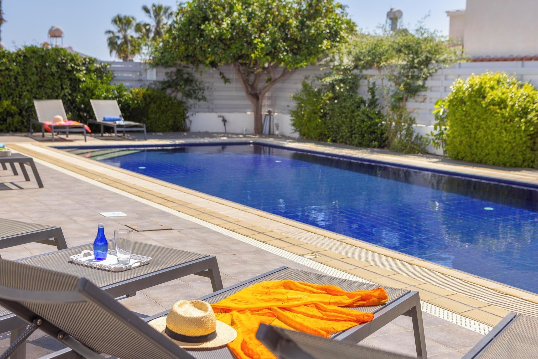 A swimming pool with lounge chairs and a table with a bottle and glass.