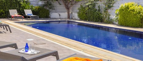 Una piscina con sillas de descanso y una mesa con una botella y un vaso.