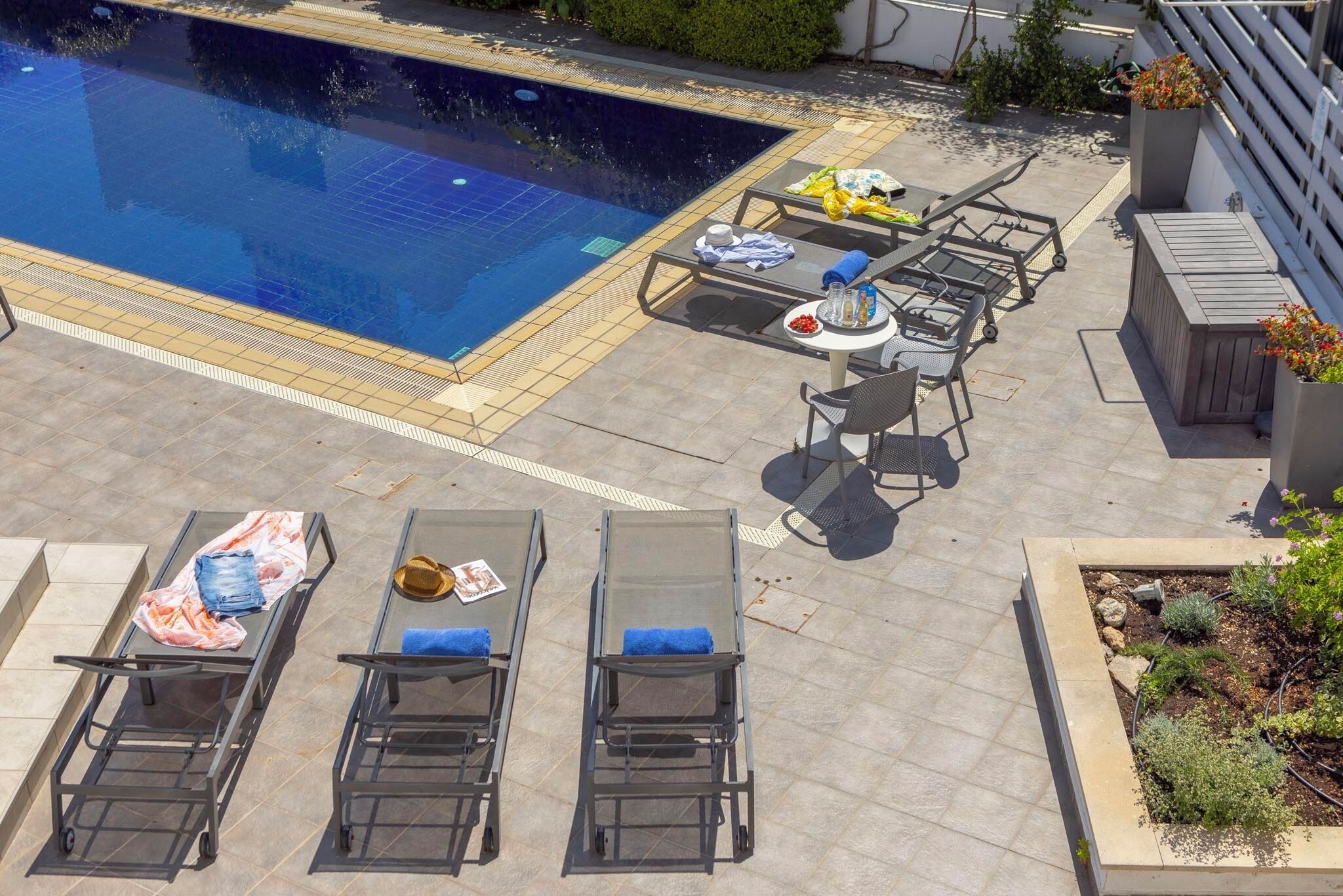 A rooftop pool area with lounge chairs, a table with drinks, and a garden bed.