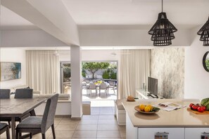 A modern living room with a dining area, a kitchen island with fresh produce, and a view to an outdoor patio. - Pantaros Luxury Villas with pool (Protaras)