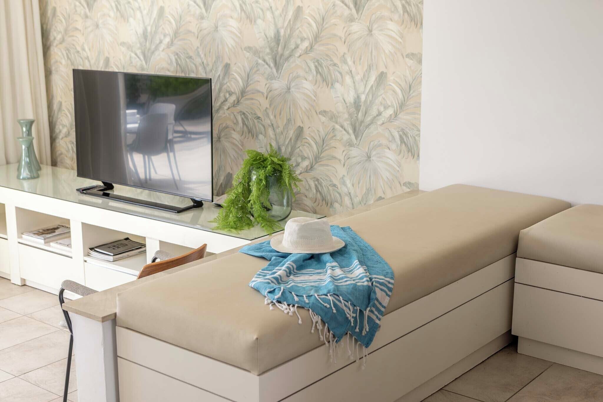 A modern living room with a sofa, a flat-screen TV, a decorative plant, and a blue and white striped throw blanket.
