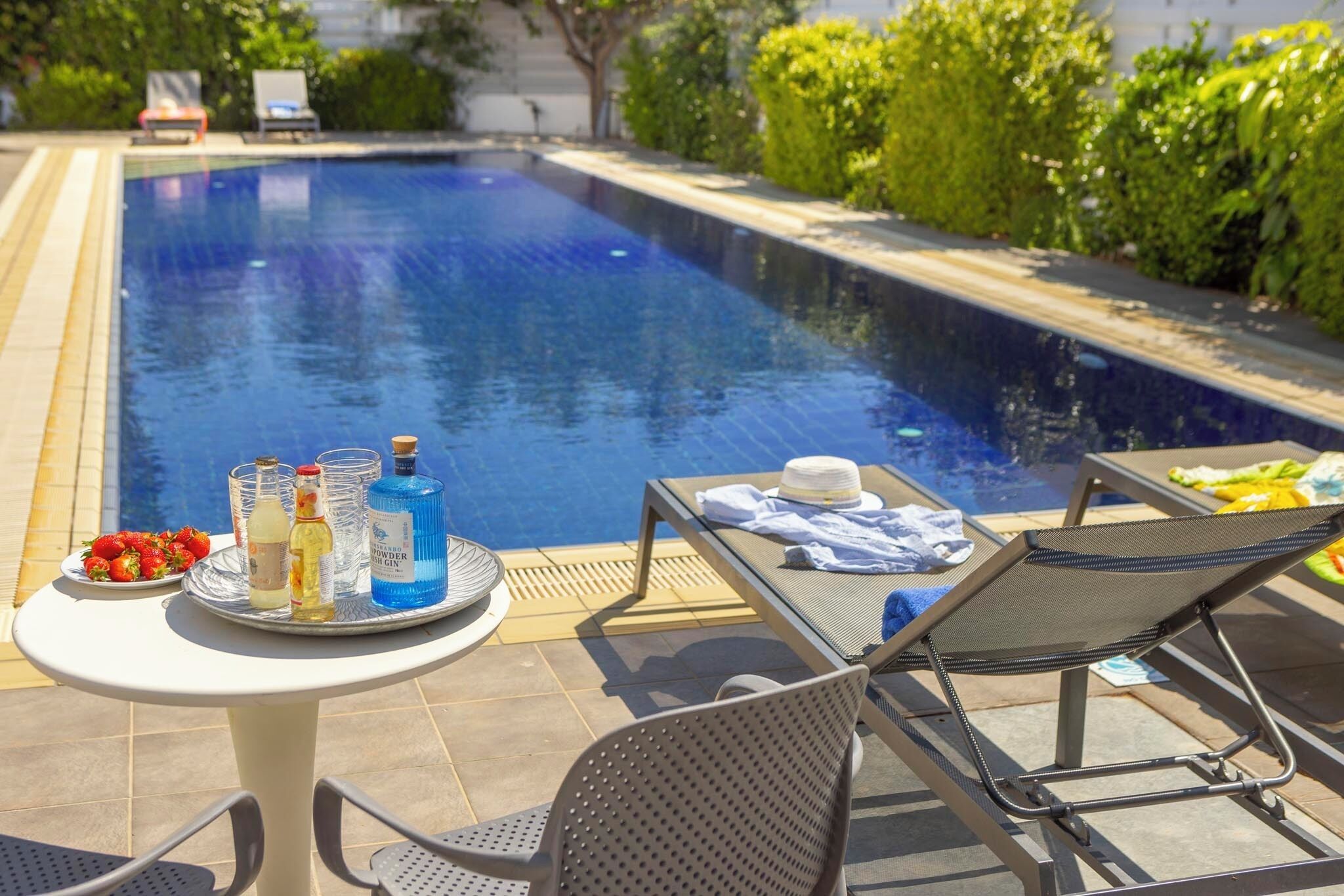 A poolside area with a table, chairs, and a tray of food and drinks.