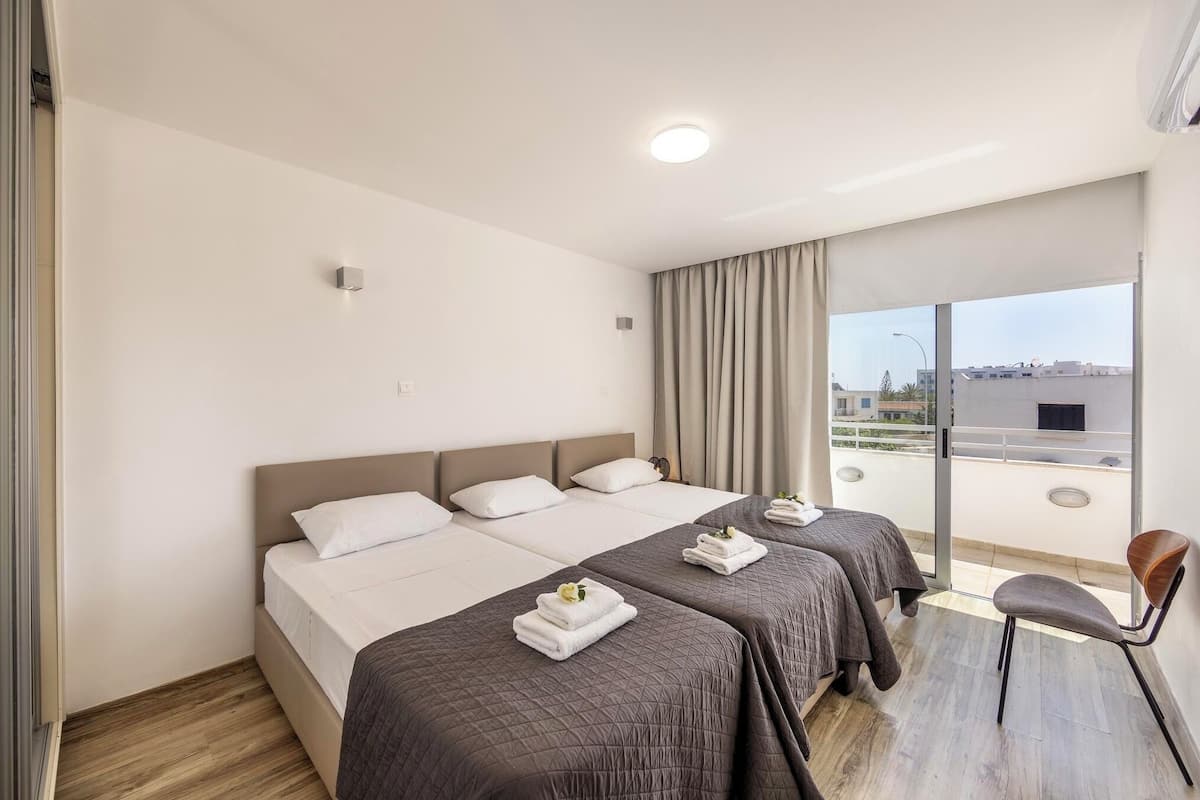 A hotel room with a large bed, two smaller beds, a chair, and a balcony with a view.