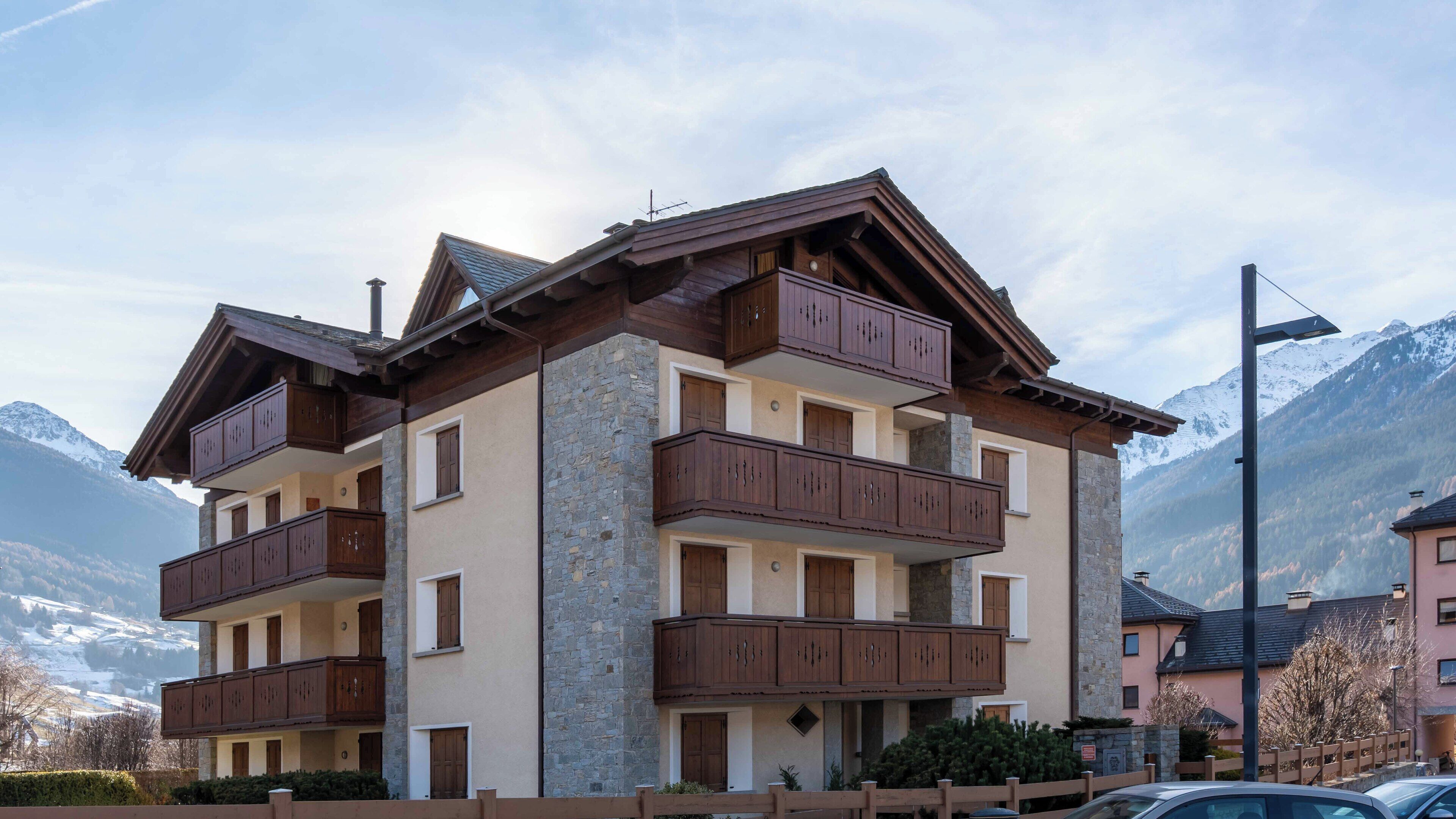 Un hotel de varios pisos con balcones, fachada de piedra y montañas al fondo.
