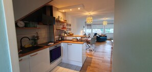 Una cocina moderna con armarios blancos, horno empotrado y encimera de madera. Cuenta con una zona de comedor con sofá azul y candelabro.