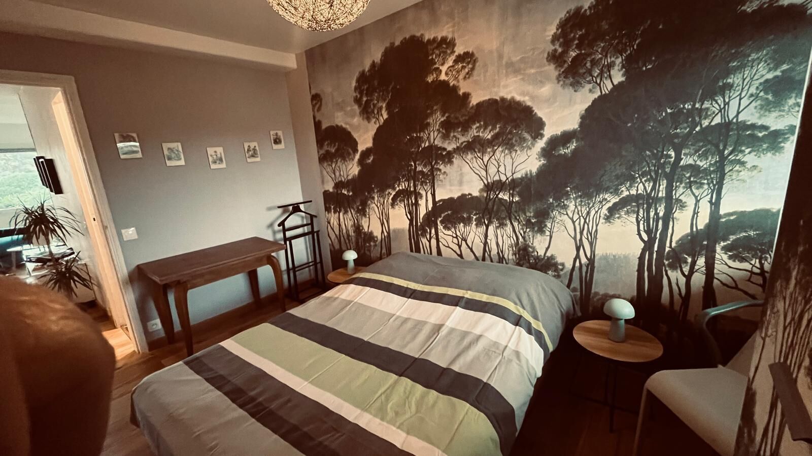 Une chambre à coucher avec un grand lit, un bureau, une chaise et une fresque murale représentant des arbres.