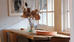 Spisebord med stole, en vase med tørrede blomster og et billede på væggen.