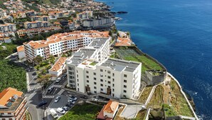 Zona residencial a la costa, amb un edifici blanc destacat que té un jardí al terrat i diversos balcons.