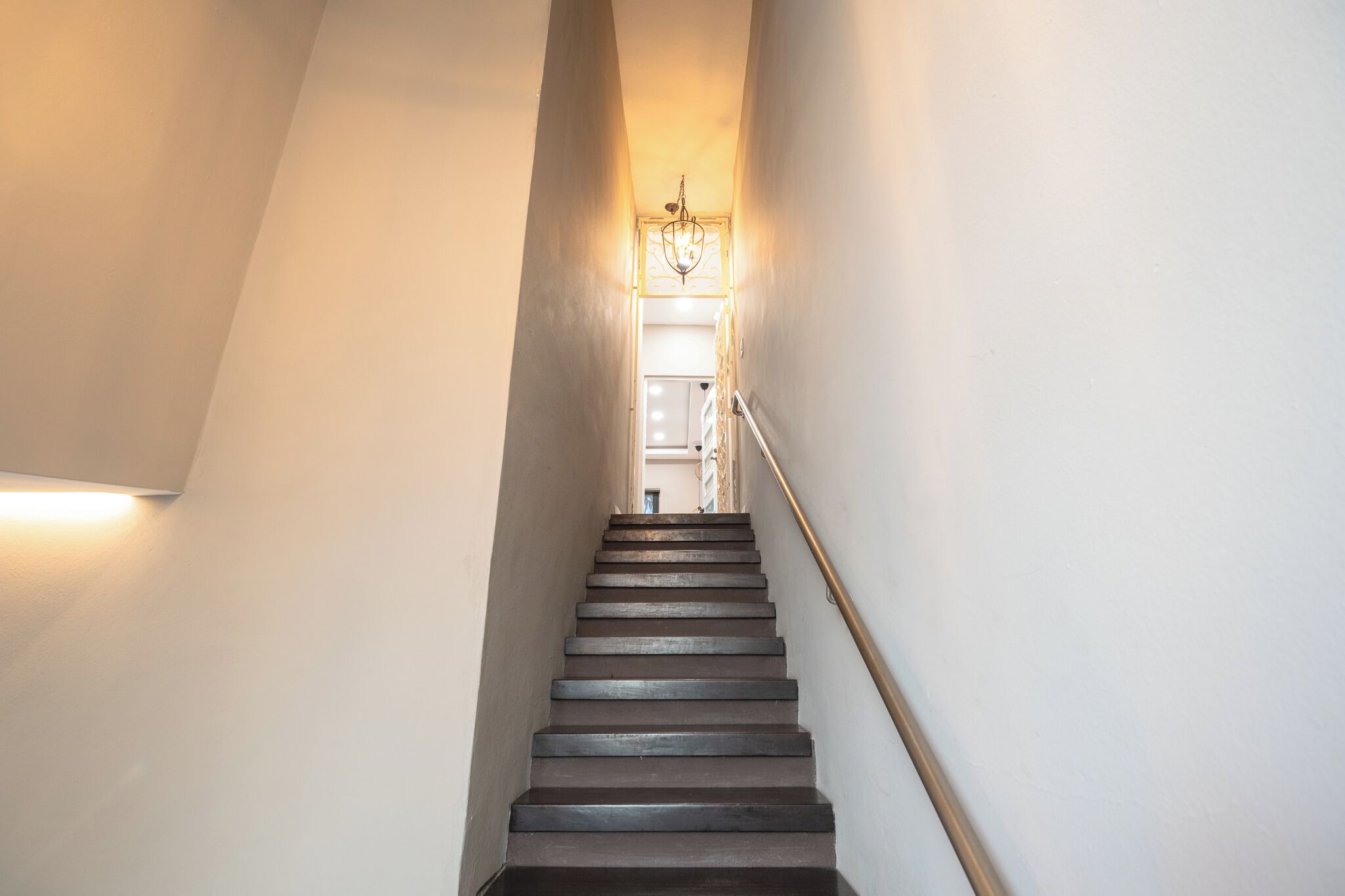 Un escalier étroit doté d’une rampe, menant à un palier sur lequel se trouve un lustre.
