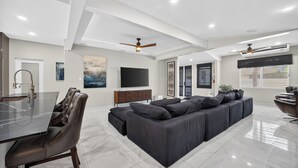 A modern living room with a large dark sofa, a dining table with chairs, a flat-screen TV, and ceiling fans. - Casa Lotus (San Juan)