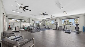 A spacious gym with ceiling fans, exercise equipment, and large windows offering views of palm trees. - Casa Lotus (San Juan)