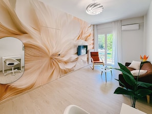 A modern living room with a large floral mural, a wooden floor, a rocking chair, a sofa, a coffee table, and a plant. - Spacious 2-bedroom apartment with AC in Nea Smirni (Nea Smirni)