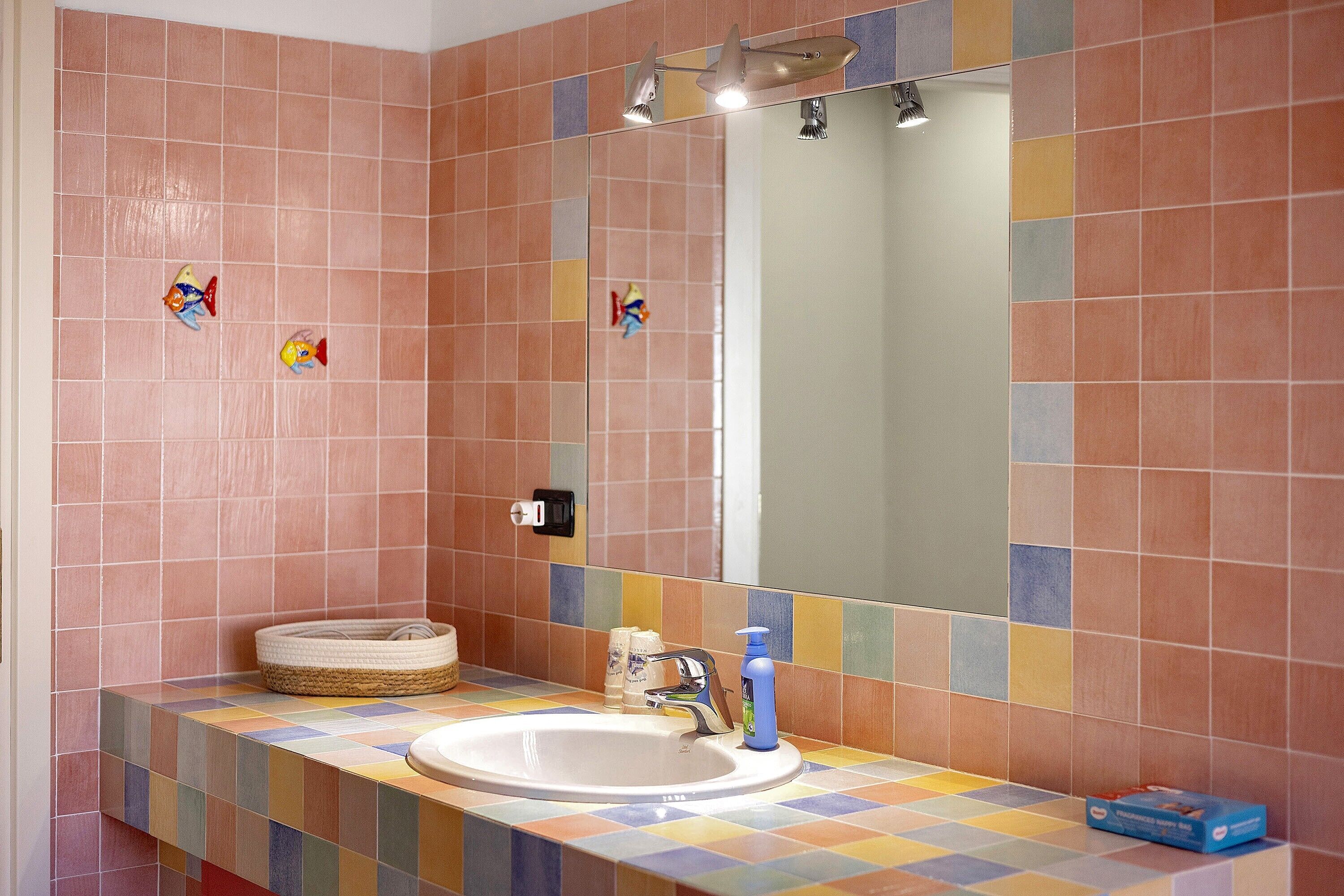 A bathroom with a tiled wall, a sink, a mirror, and a towel rack.