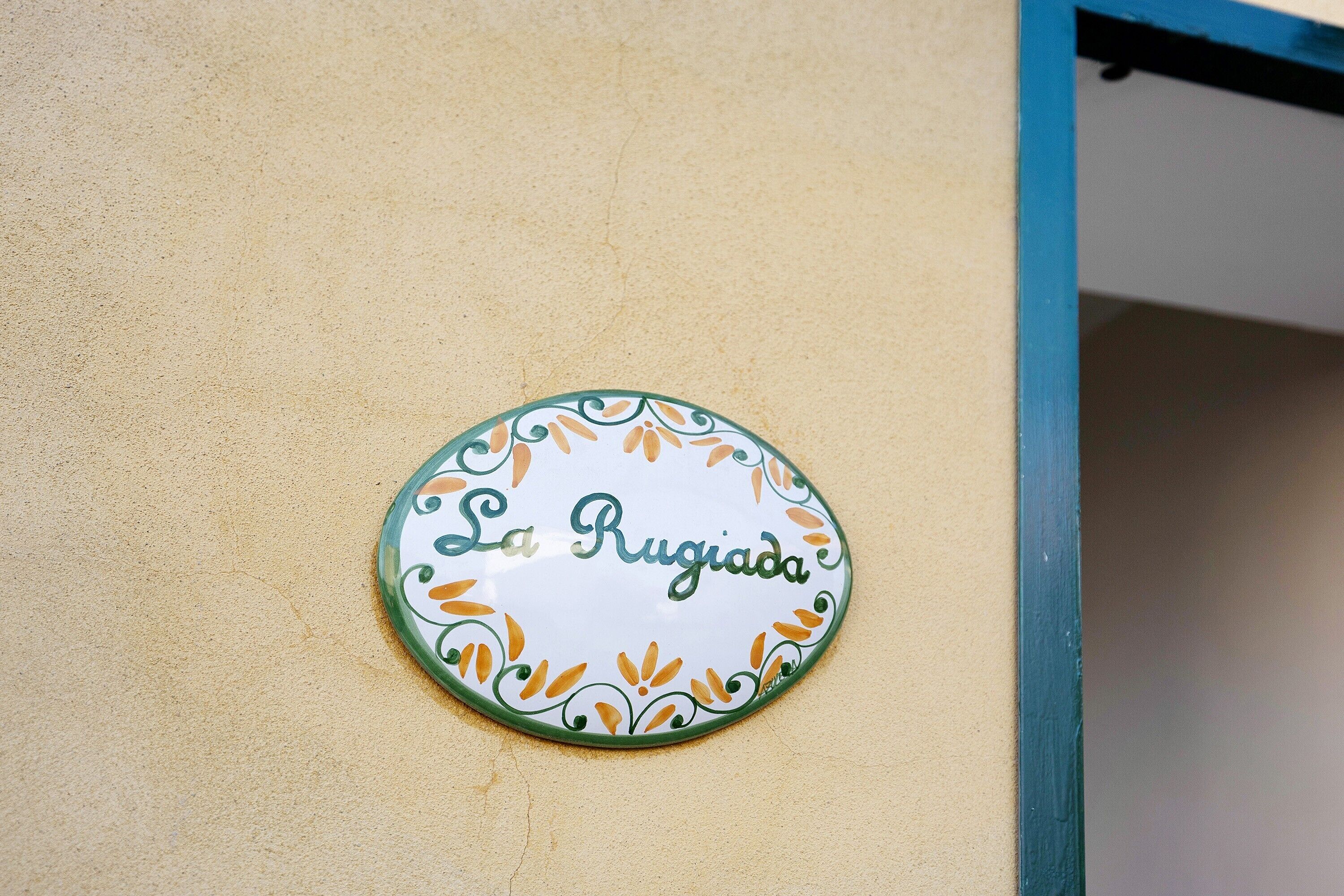 A round sign with 'La Rugiada' text on a beige wall.
