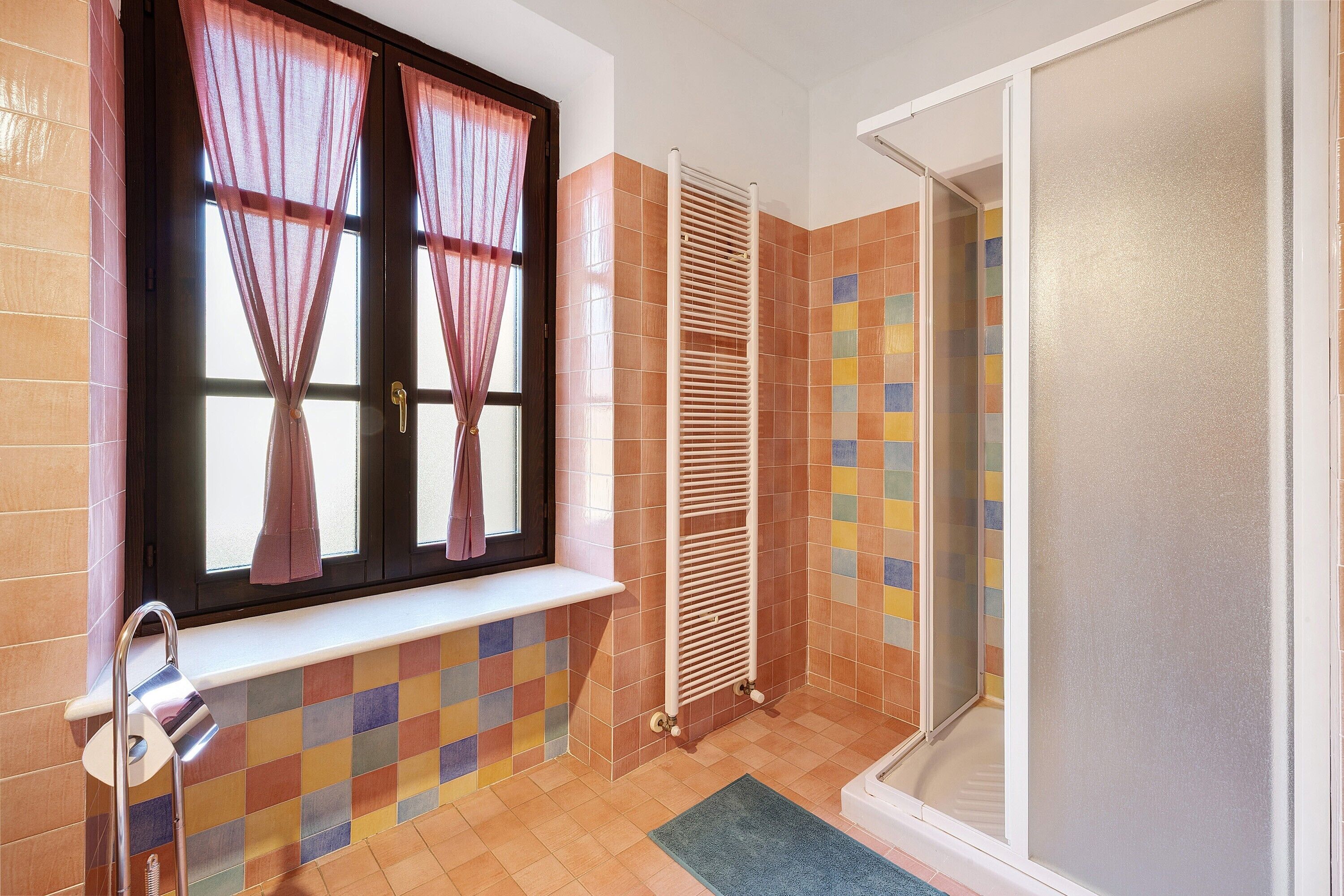 A bathroom with a window, a towel rack, a shower, and a tiled floor.