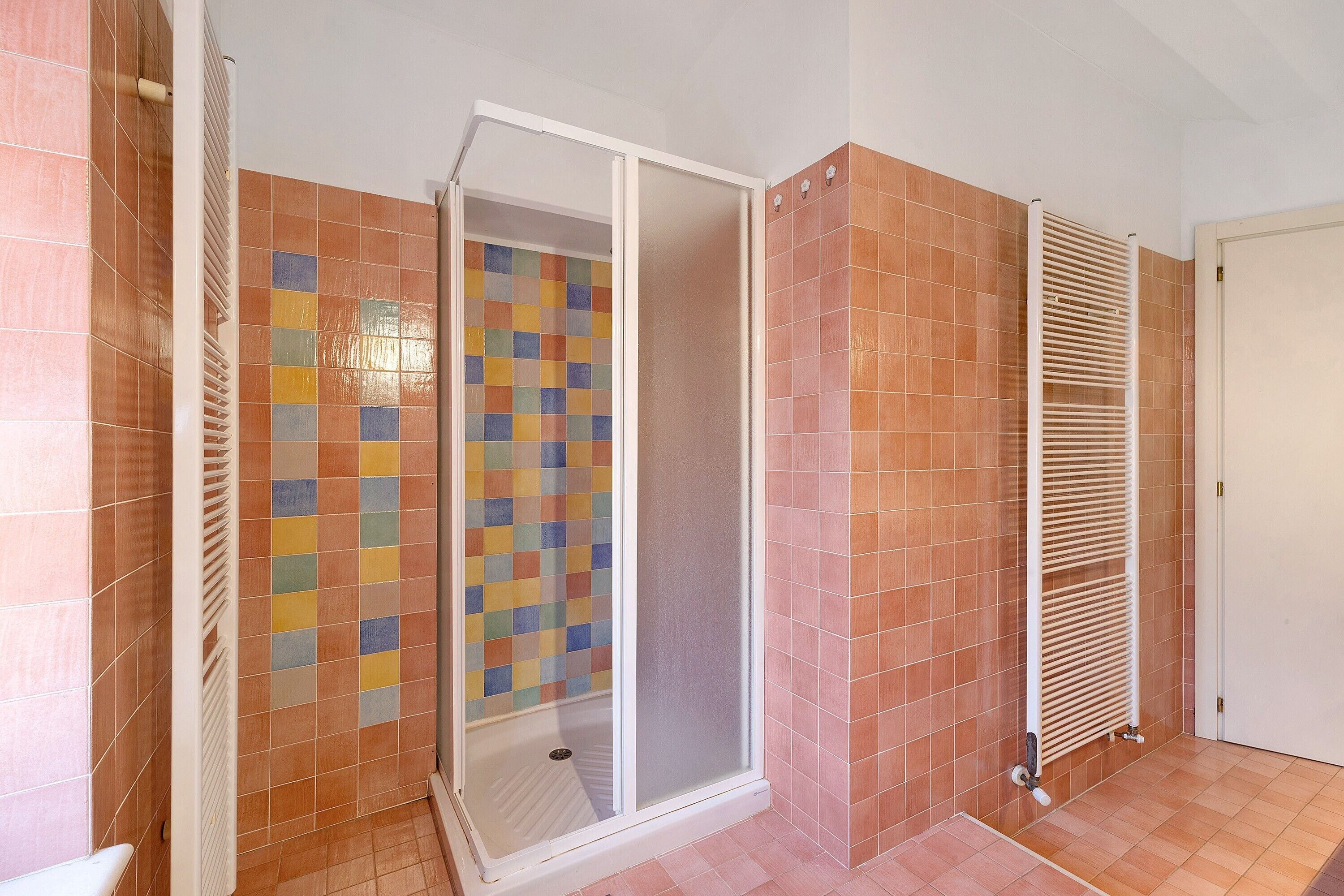 Une salle de bain avec une douche, des murs carrelés et un radiateur.