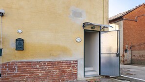 A building with a yellow wall, a brick base, and a metal door. - B&B La Rugiada with Wi-Fi (Pratomorone)