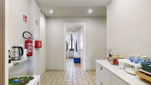 A narrow hallway with a fire extinguisher, a coffee maker, and a refrigerator on the left. A bed is visible in the distance. - B&B La Rugiada with Wi-Fi (Pratomorone)