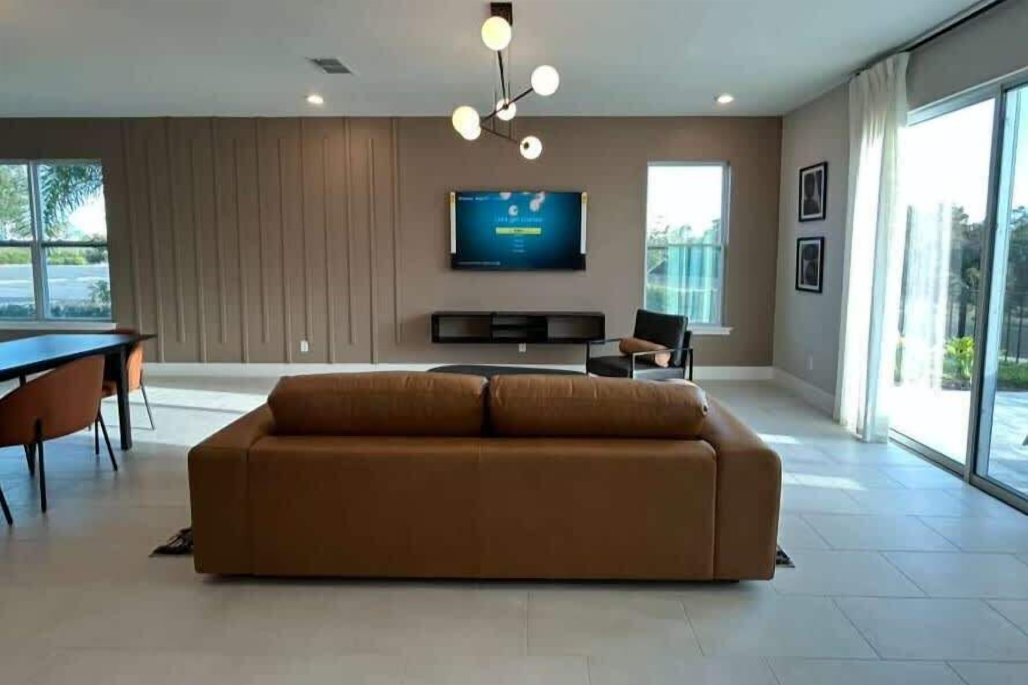 Een moderne woonkamer met een grote bruine bank, een flatscreen televisie aan de muur en een eethoek met een tafel en stoelen.