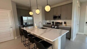 Una cocina moderna con una isla grande, taburetes de bar e iluminación colgante.