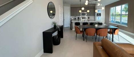 A modern kitchen with a dining area, a sofa, and a large window.