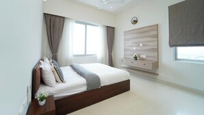 A modern bedroom with a large bed, a ceiling fan, a TV, and a window with curtains. - Auric Blue by Red Olive3bhkomrprime IT Corner (Chennai)