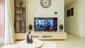 A modern living room with a flat-screen TV on a white entertainment unit, a round coffee table, and a decorative vase. - Auric Blue by Red Olive3bhkomrprime IT Corner (Chennai)