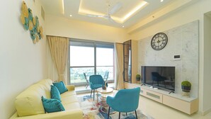 A modern living room with a sofa, chairs, a TV, and a large window. - Auric Blue by Red Olive3bhkomrprime IT Corner (Chennai)