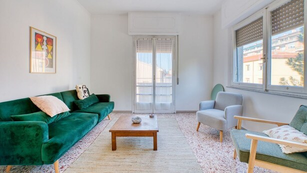 Una sala de estar con un sofá verde, una mesa de centro de madera, un sillón gris y una ventana con persianas.