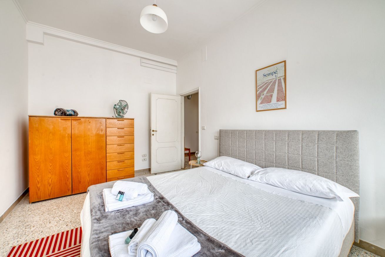 Una habitación de hotel con una cama, un armario de madera, un tapete rojo y blanco a rayas y un cuadro en la pared.
