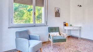 Una habitación con ventana, una silla, un escritorio y un cuadro en la pared.