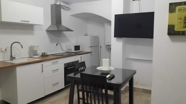 A compact kitchen with white cabinets, a wooden countertop, a black stove, and a black dining table with two chairs. - Central 1-Bedroom Apartment in Historic Úbeda-Aurora1 (Úbeda)