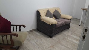 A small, cozy room with a beige sofa, a wooden chair, and a small table. - Central 1-Bedroom Apartment in Historic Úbeda-Aurora1 (Úbeda)