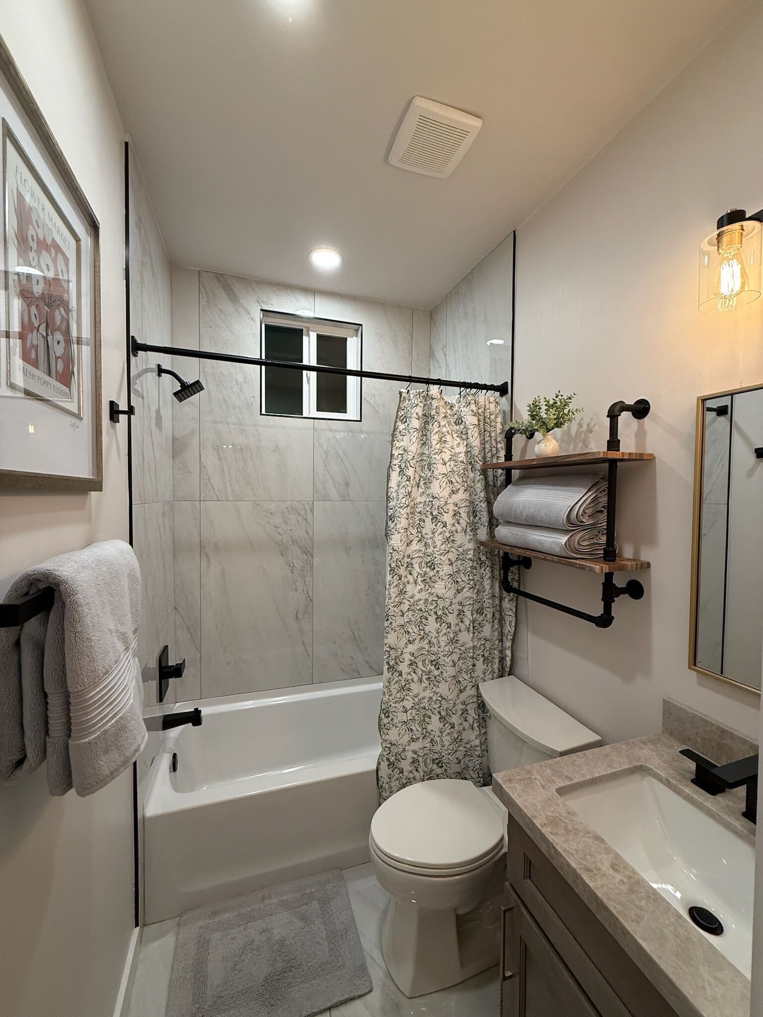 A modern bathroom with a bathtub, toilet, and sink. There is a shower curtain, a towel rack, and a mirror.