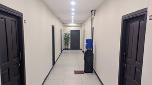 A long, narrow hallway with black doors on both sides, a tiled floor, and a ceiling with recessed lighting. - Nathan Residency (Tiruchirappalli)