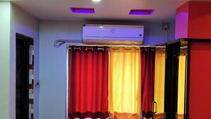 A room with a ceiling-mounted air conditioner, a curtain with red and yellow panels, and a red wall. - Hotel Tulusi Inn (Bolpur)