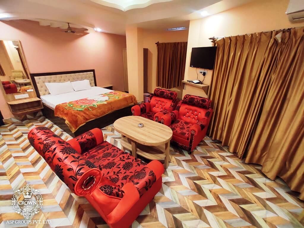 A hotel room with a bed, a sofa, a chair, a small table, and a television.