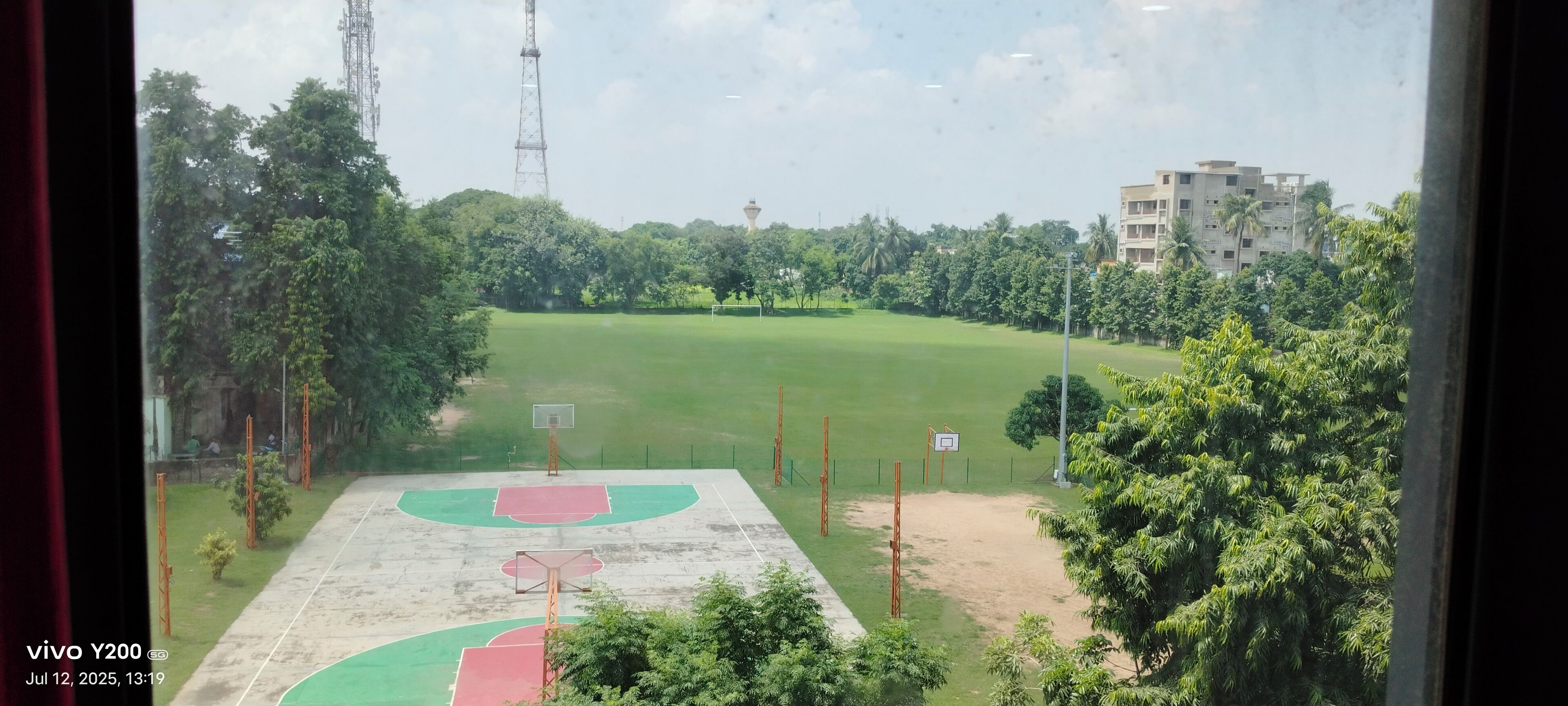 A basketball court with a green and red playing surface, surrounded by trees and buildings.