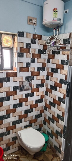 Um banheiro com parede revestida de azulejos, vaso sanitário, lixeira verde e aquecedor de água fixado na parede.