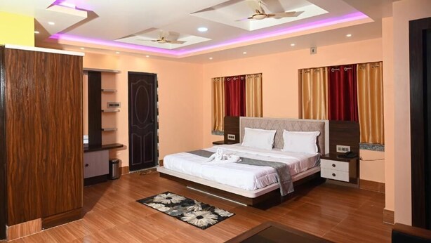 A modern hotel room with a large bed, a wooden wardrobe, a small desk, and a ceiling fan. - Hotel Tulusi Inn (Bolpur)