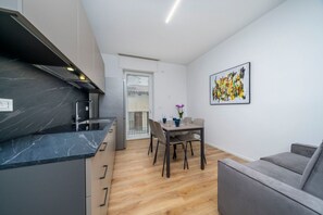 Una cocina moderna con encimera de mármol, un comedor con mesa y sillas, y un sofá gris.