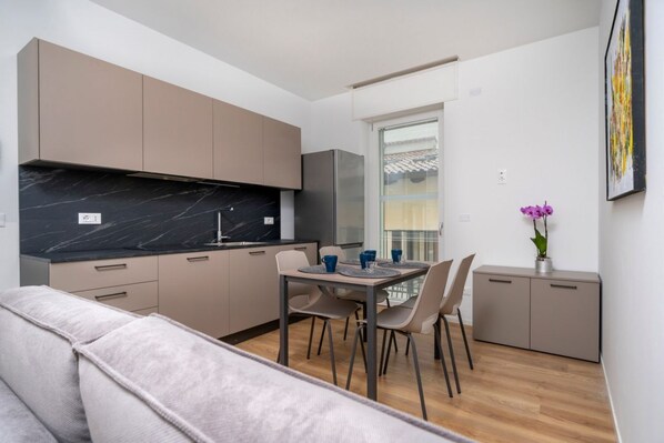 Una cocina moderna con encimera de mármol, una zona de comedor con mesa y sillas, y un sofá gris.