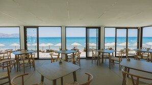 A beachside restaurant with tables and chairs, large windows, and beach umbrellas. - Casa di Notos Beach Hotel-Georgioupolis (Apokoronas)